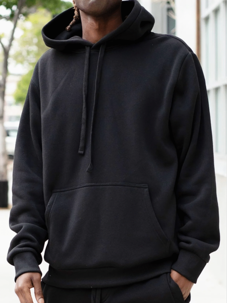 Man wearing plain black hoodie with front pocket and drawstrings, in a streetwear setting.