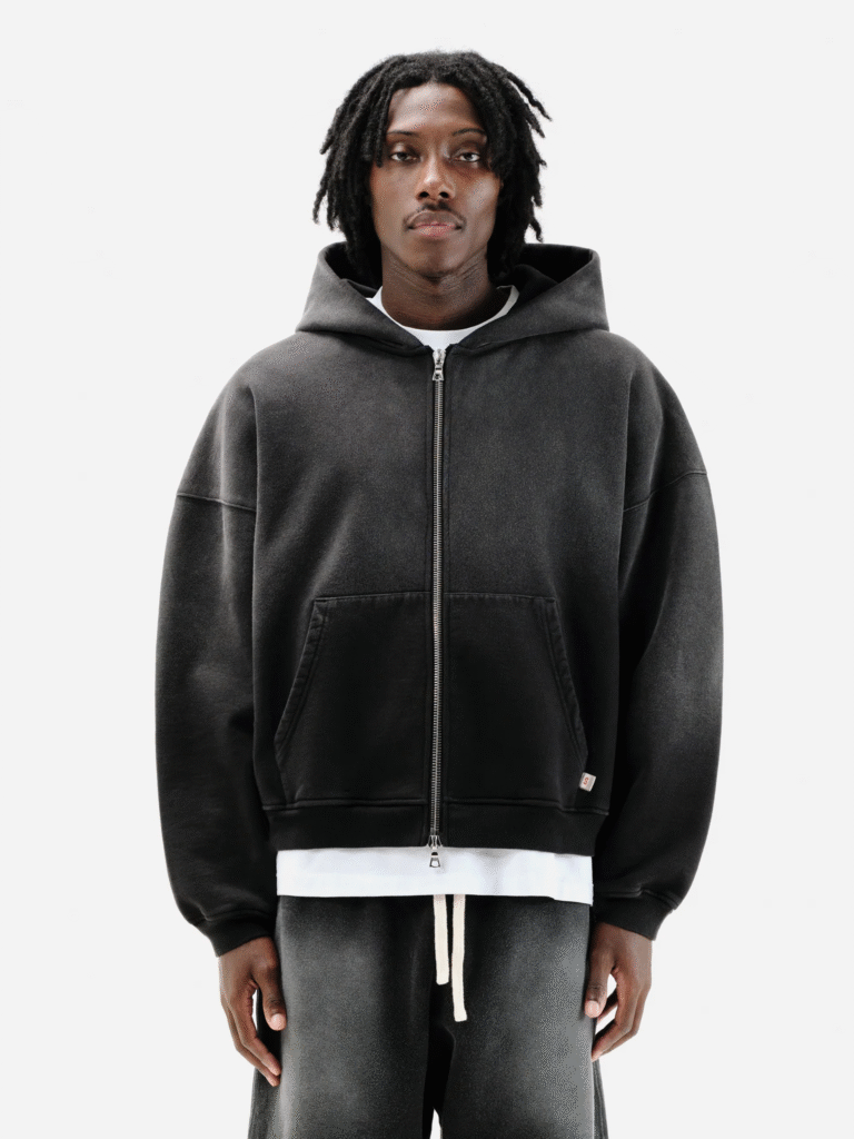 Man in faded black zip-up hoodie and matching sweatpants, styled with white layering and relaxed fit.