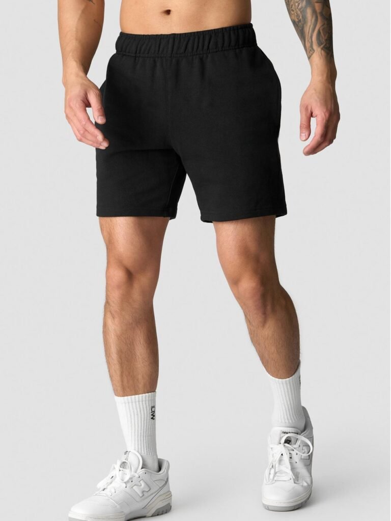 Man wearing plain black athletic sweat shorts with an elastic waistband, paired with white crew socks and white sneakers. A clean and minimal workout or casual outfit.