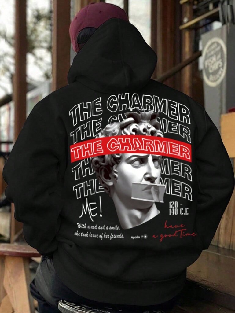 Person wearing black hoodie with bold “THE CHARMER” text and statue print design, featuring artistic streetwear style