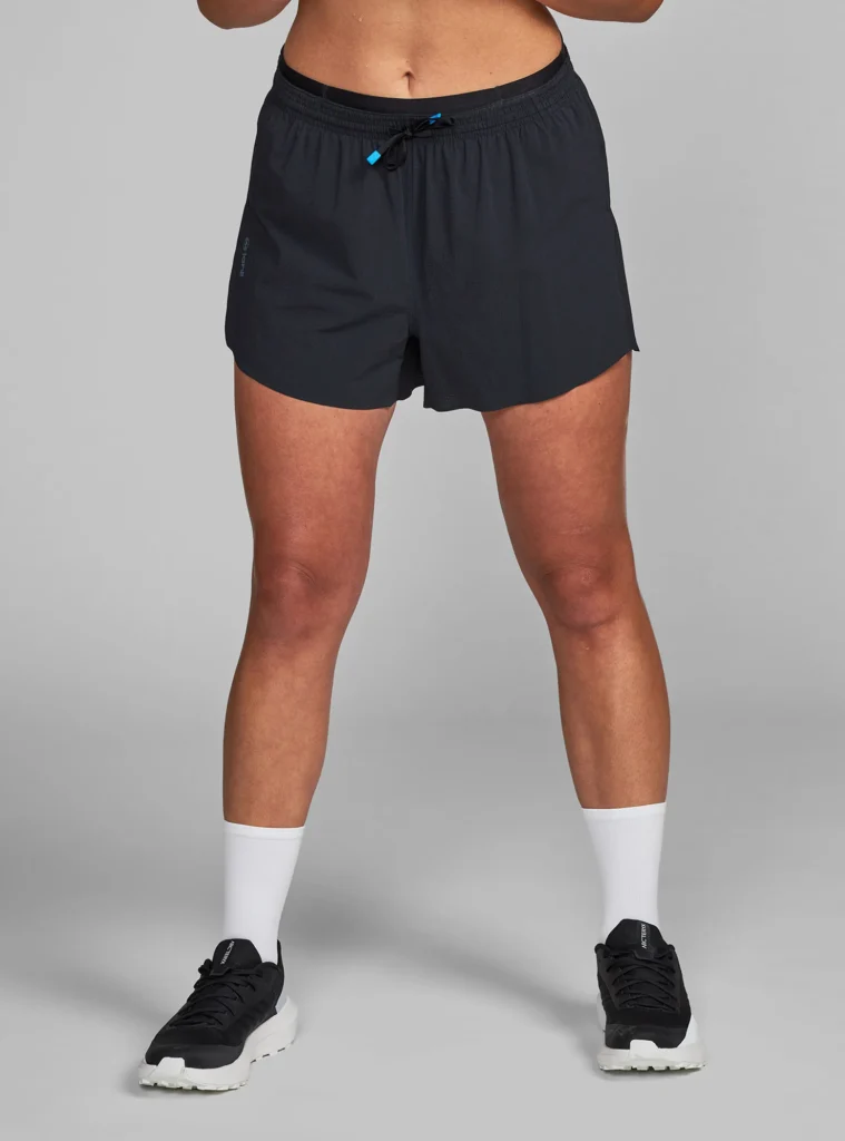 Woman wearing lightweight black running shorts with drawstring waist, paired with white socks and black sneakers.