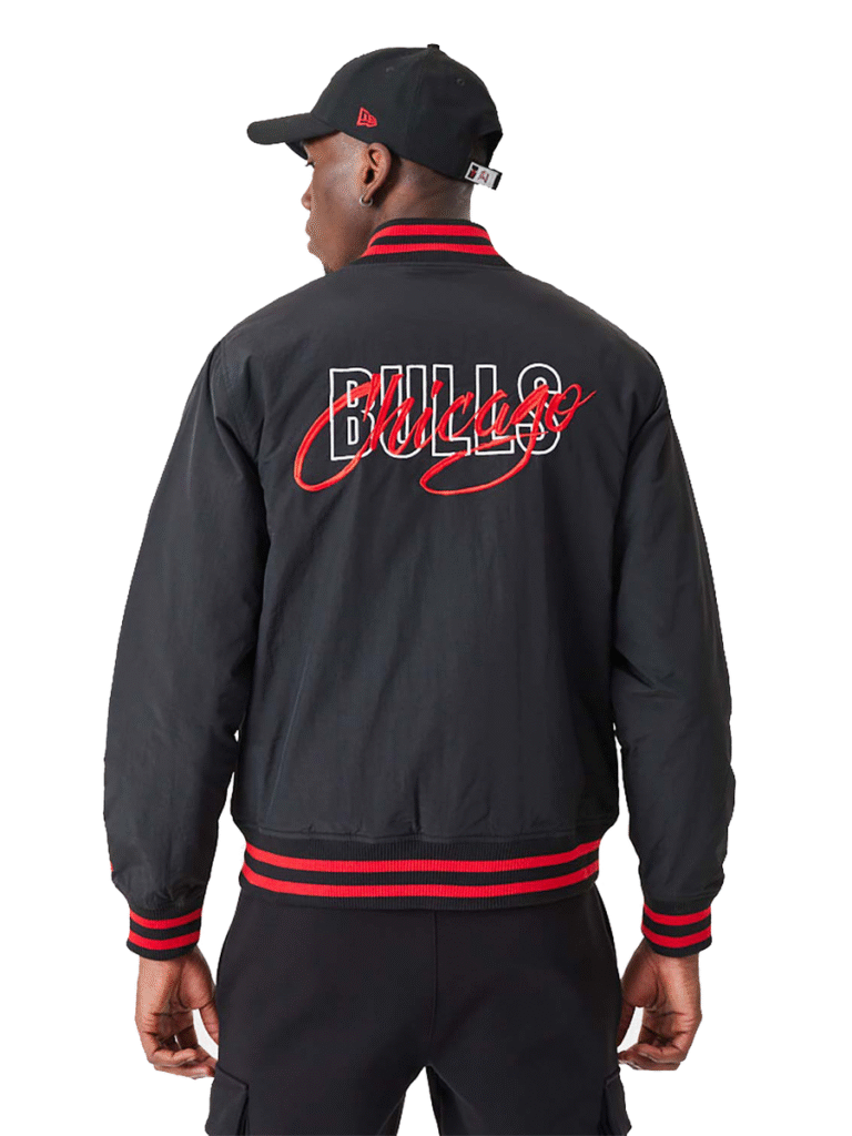 Man wearing black varsity-style jacket with red and white "Chicago Bulls" embroidery on the back, paired with a black cap and black pants.