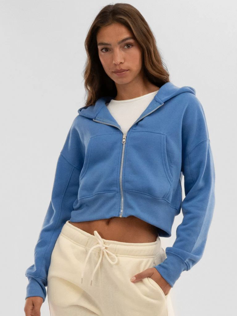 Woman wearing cropped blue zip-up hoodie with white drawstring sweatpants and casual layering style
